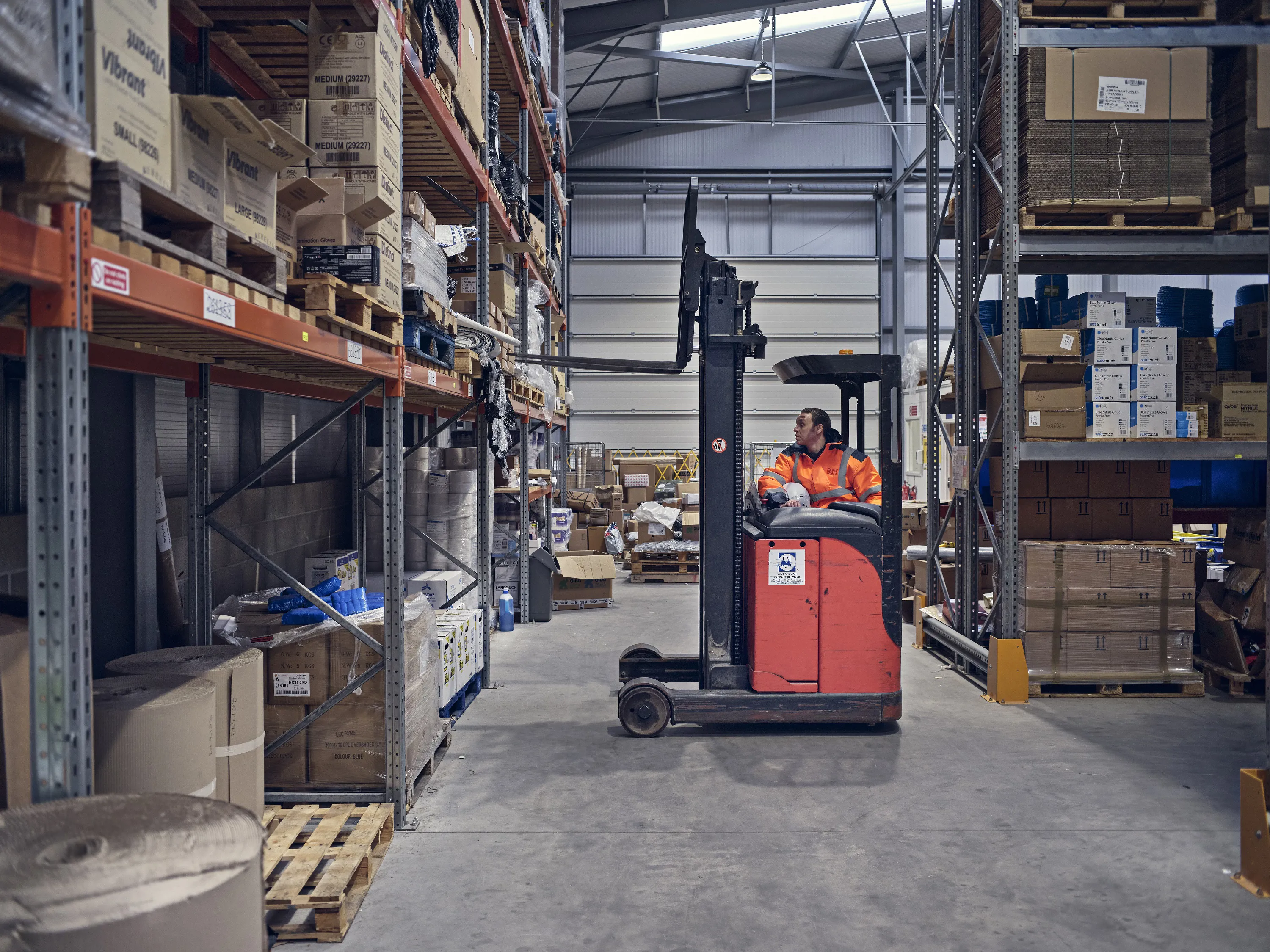Warehouse employee in high vis jacket operating a fork lift