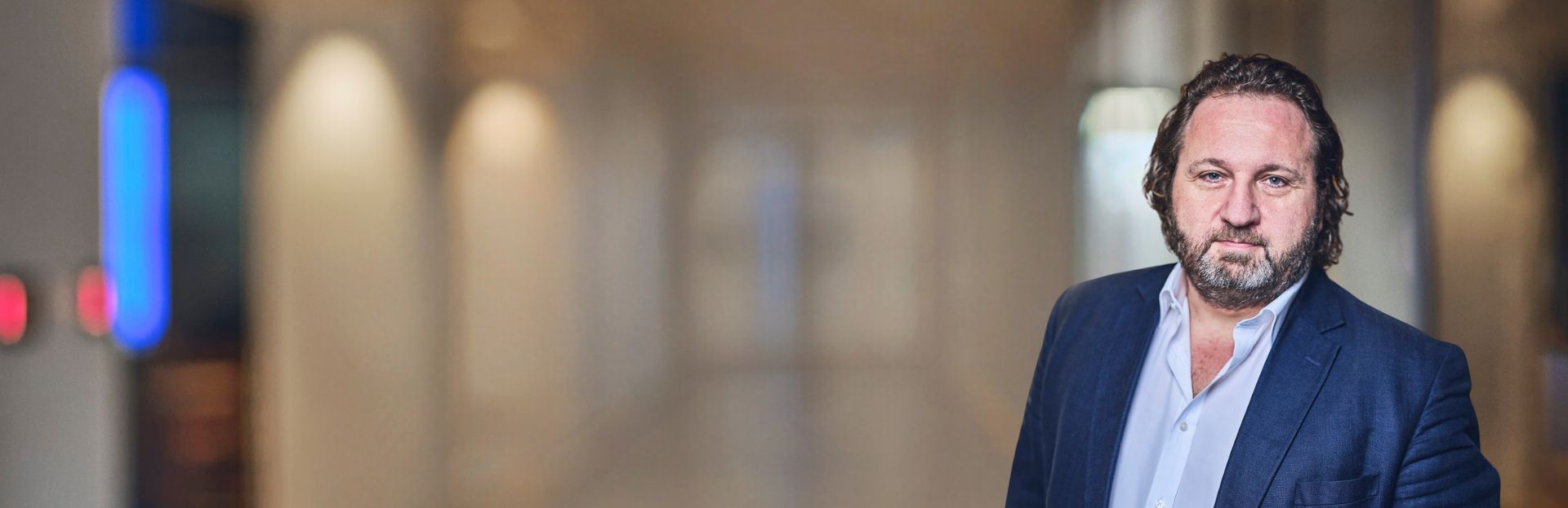 Man in a suit, standing in a blurred hallway.