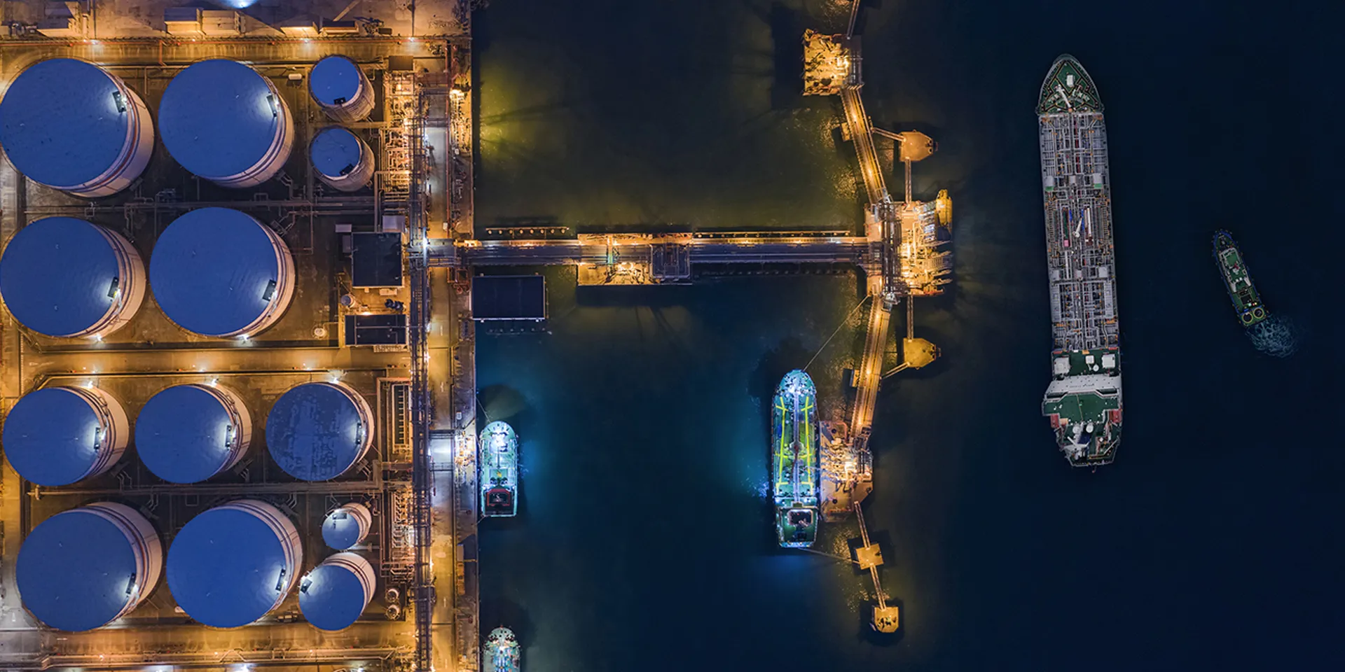 Aerial top view Tugboat pulling Oil ship tanker to loading dock at night for load or unload oil to refinery on the sea
