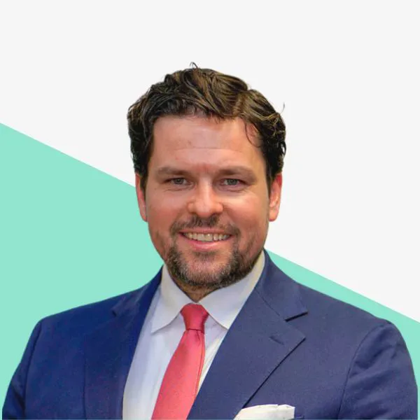 Man in a suit smiling against a light background.