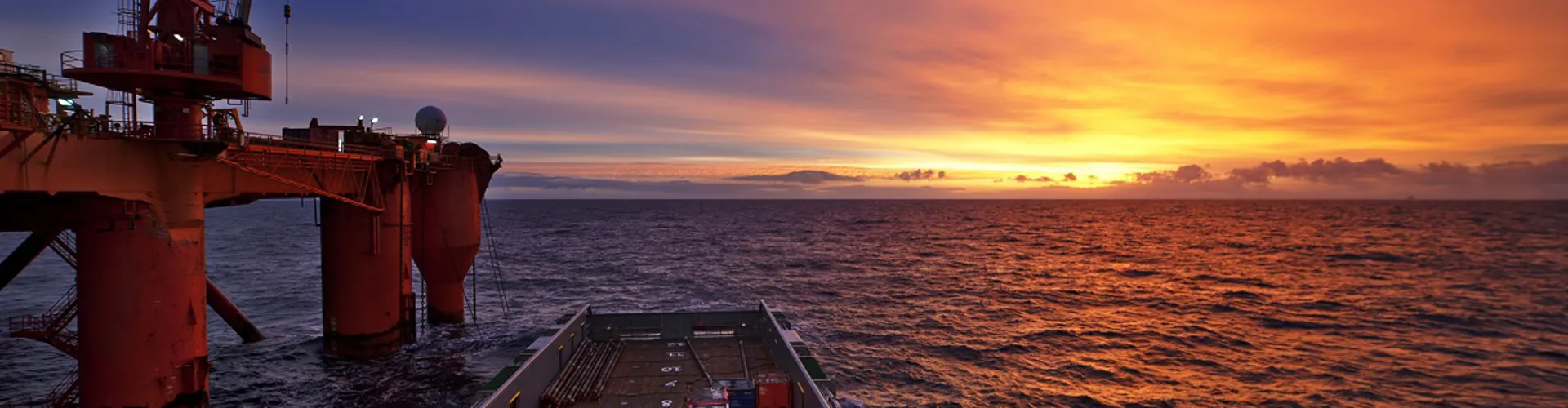 Oil rig at sunset over calm ocean waters.