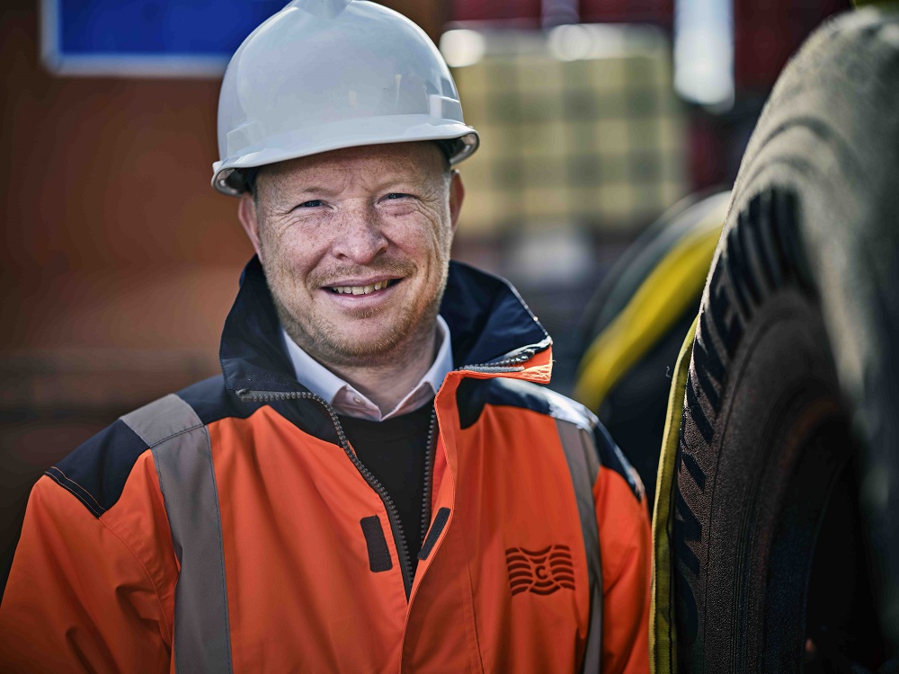Person in safety gear smiling near tires.
