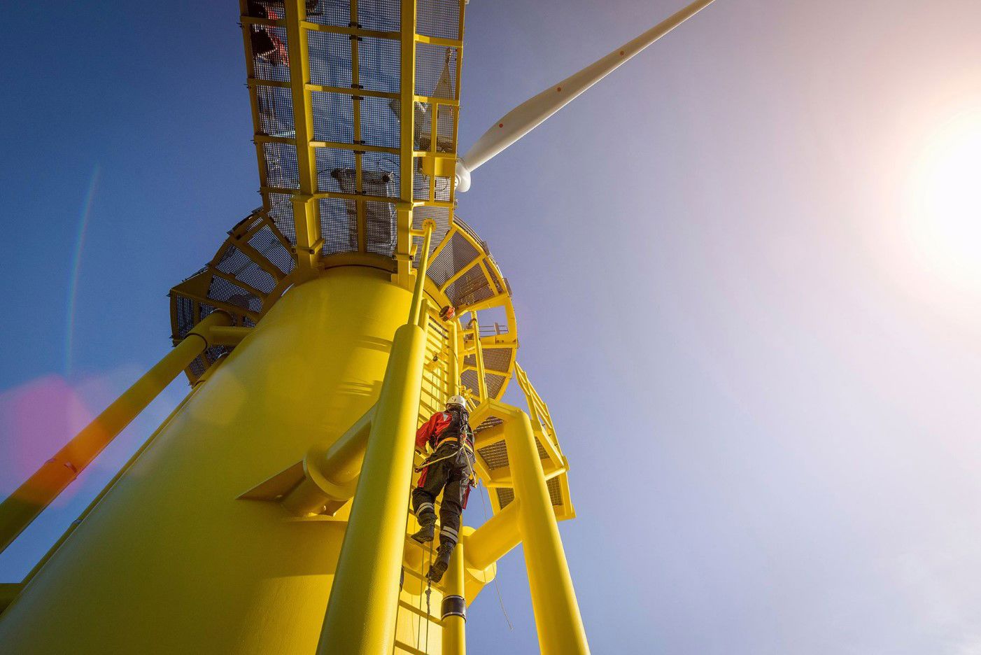 Engineers climbing wind turbine from boat at offshore windfarm, low angle view