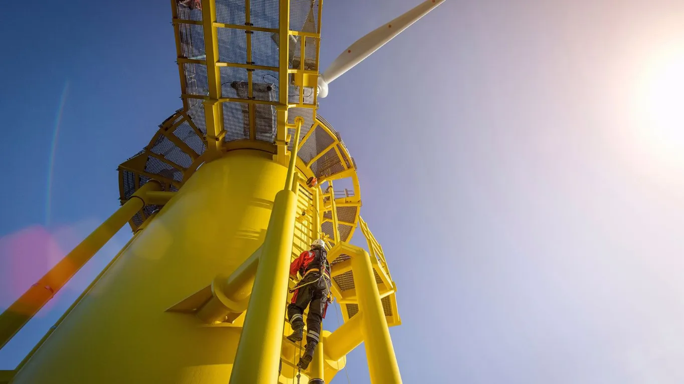 Worker climbing a yellow wind turbine tower.