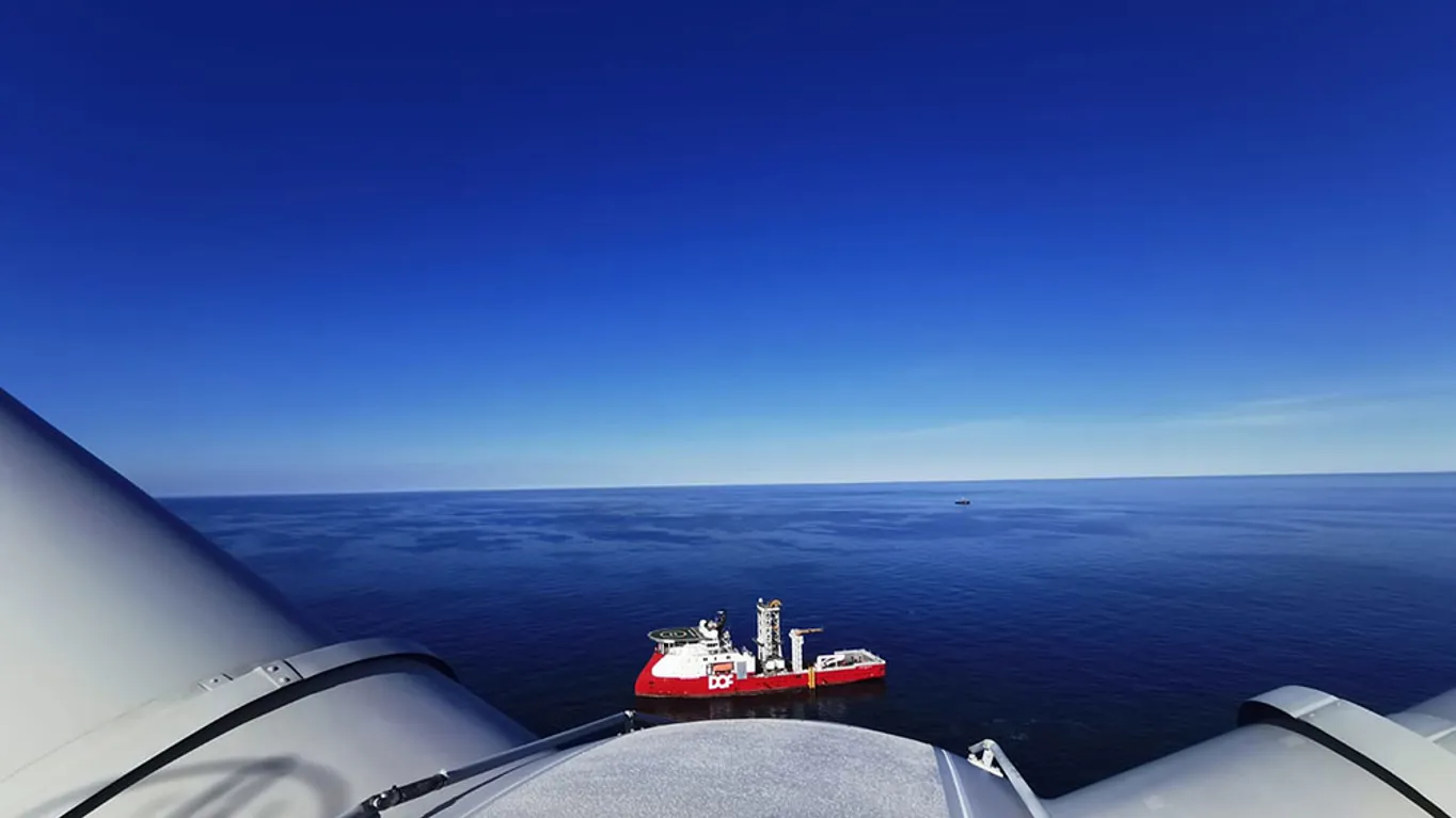 top of a wind turbine with a boat in the background