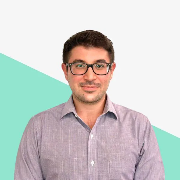 Man with glasses smiling against a light backdrop.