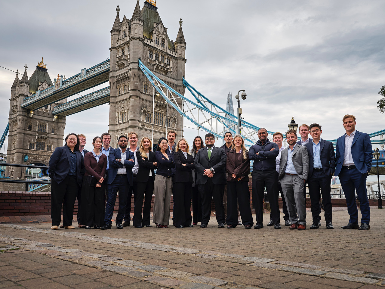 Group of 20 people in business attire posing in front of London's Tower Bridge.