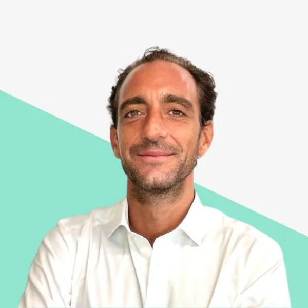 Man in a white shirt smiling against a light background.