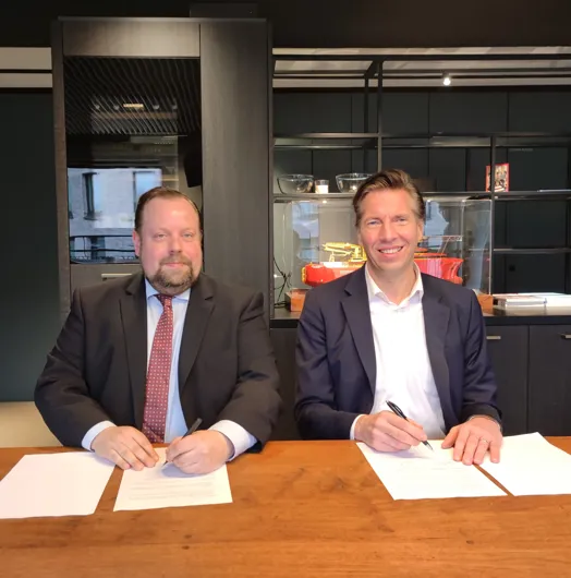 two men sitting at a table signing documents