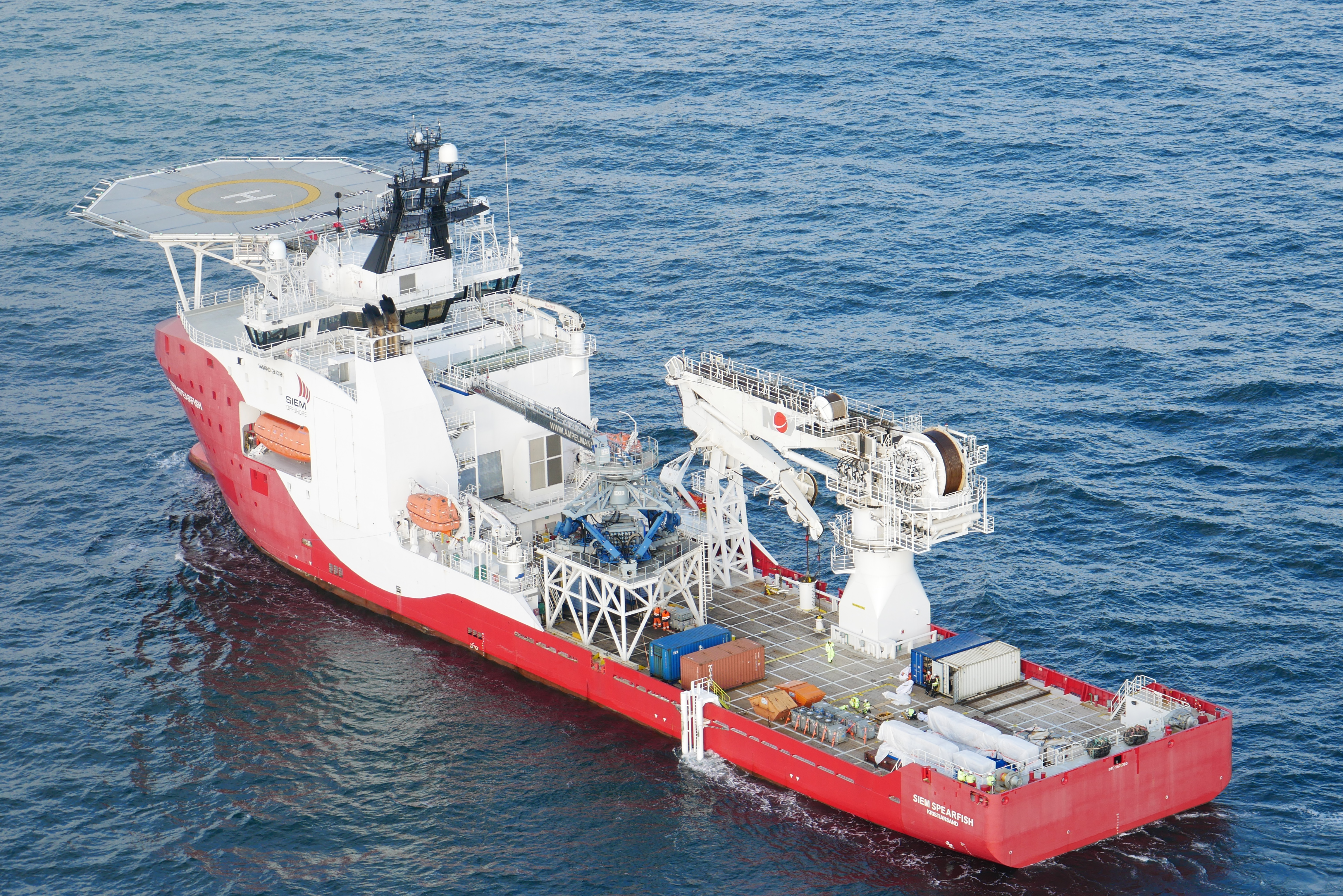Large multi-deck vessel with a red and white hull on the water, featuring a helipad and crane.