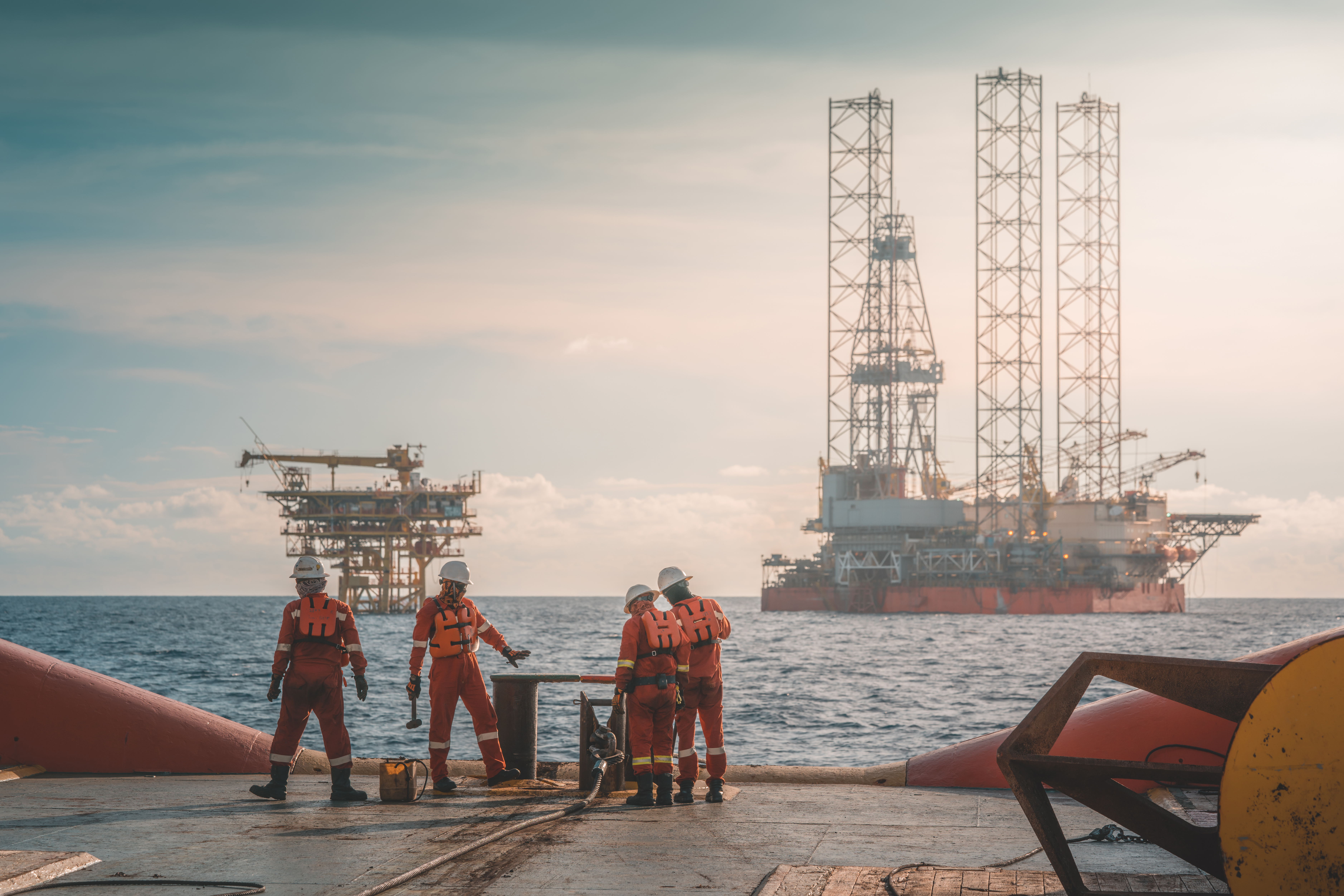 Workers on a platform with oil rigs in background.