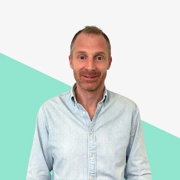 Man smiling in a light blue shirt against a pastel background.