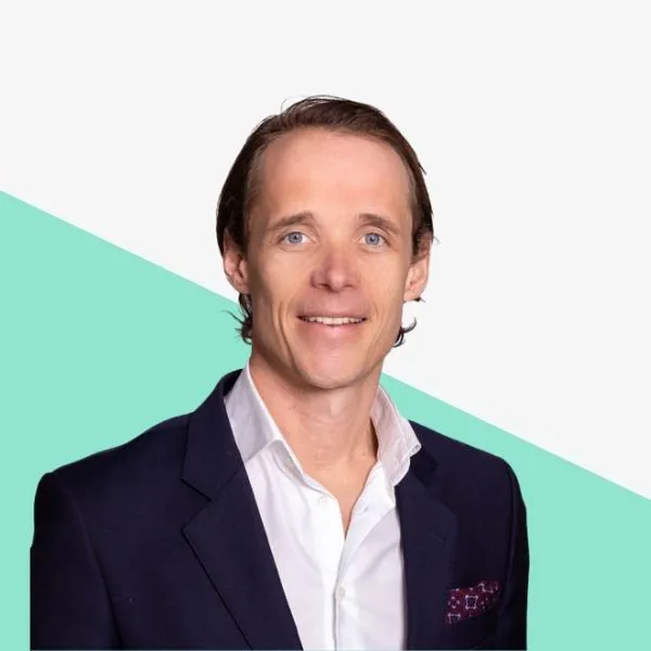 Man in a blazer smiling against a light background.