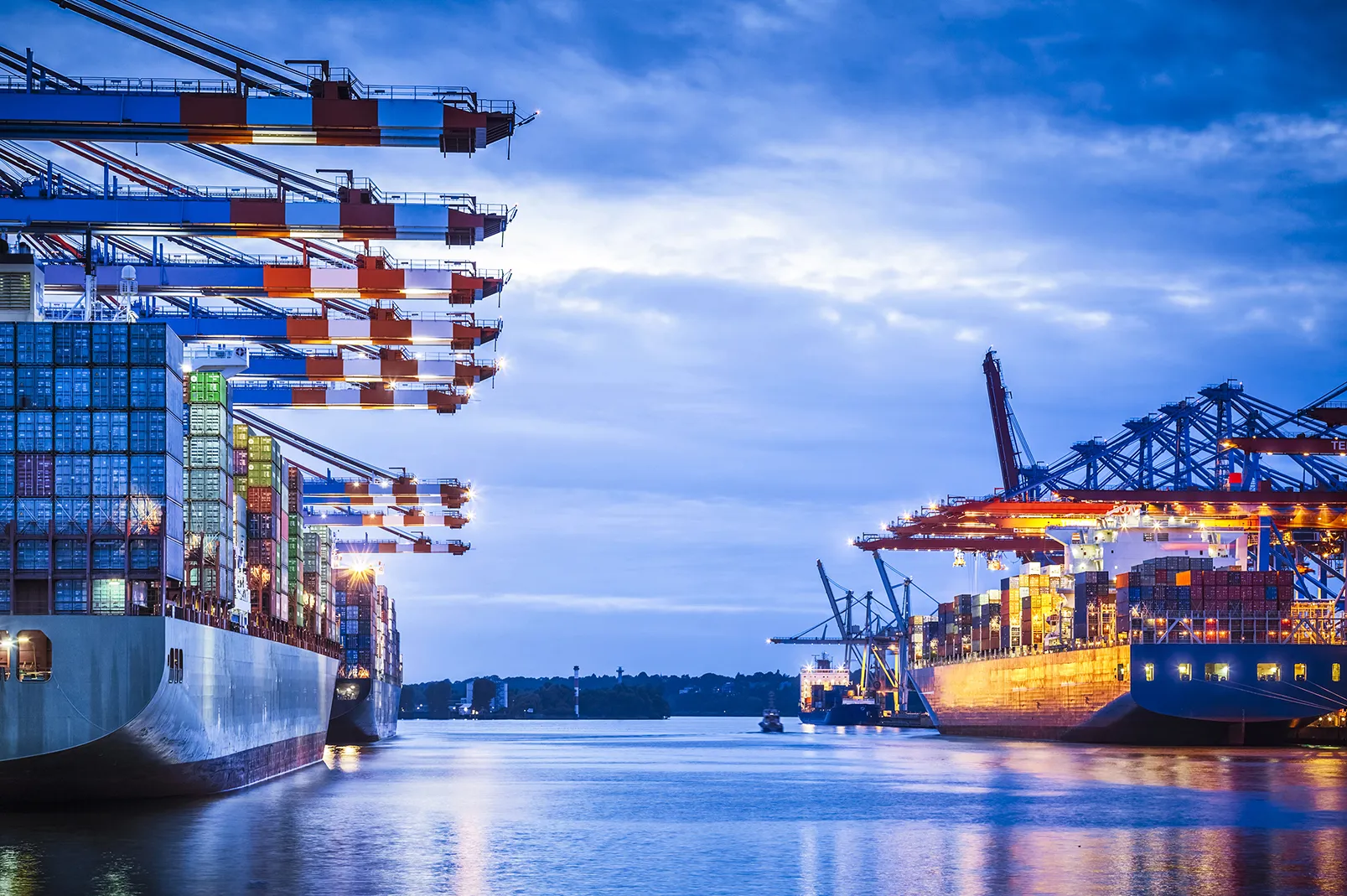 Container ships at a bustling port at dusk.
