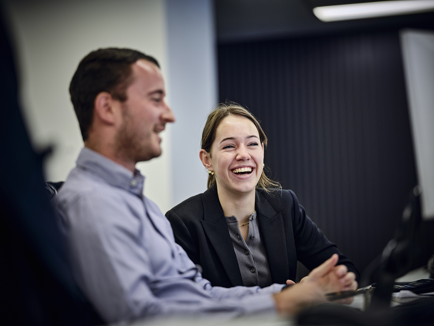 focus on woman smiling at desk whilst discussing with a colleague