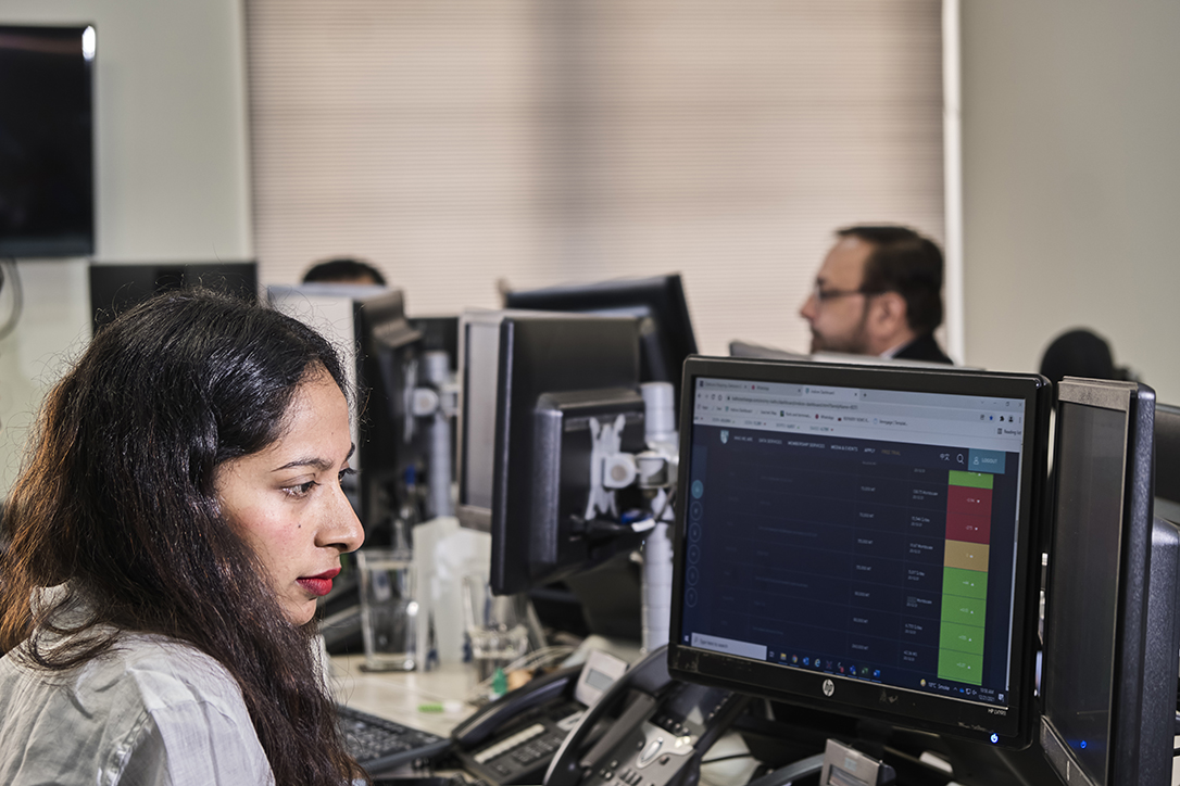 Woman with dark hair at a desk focused on multiple computer monitors with data.