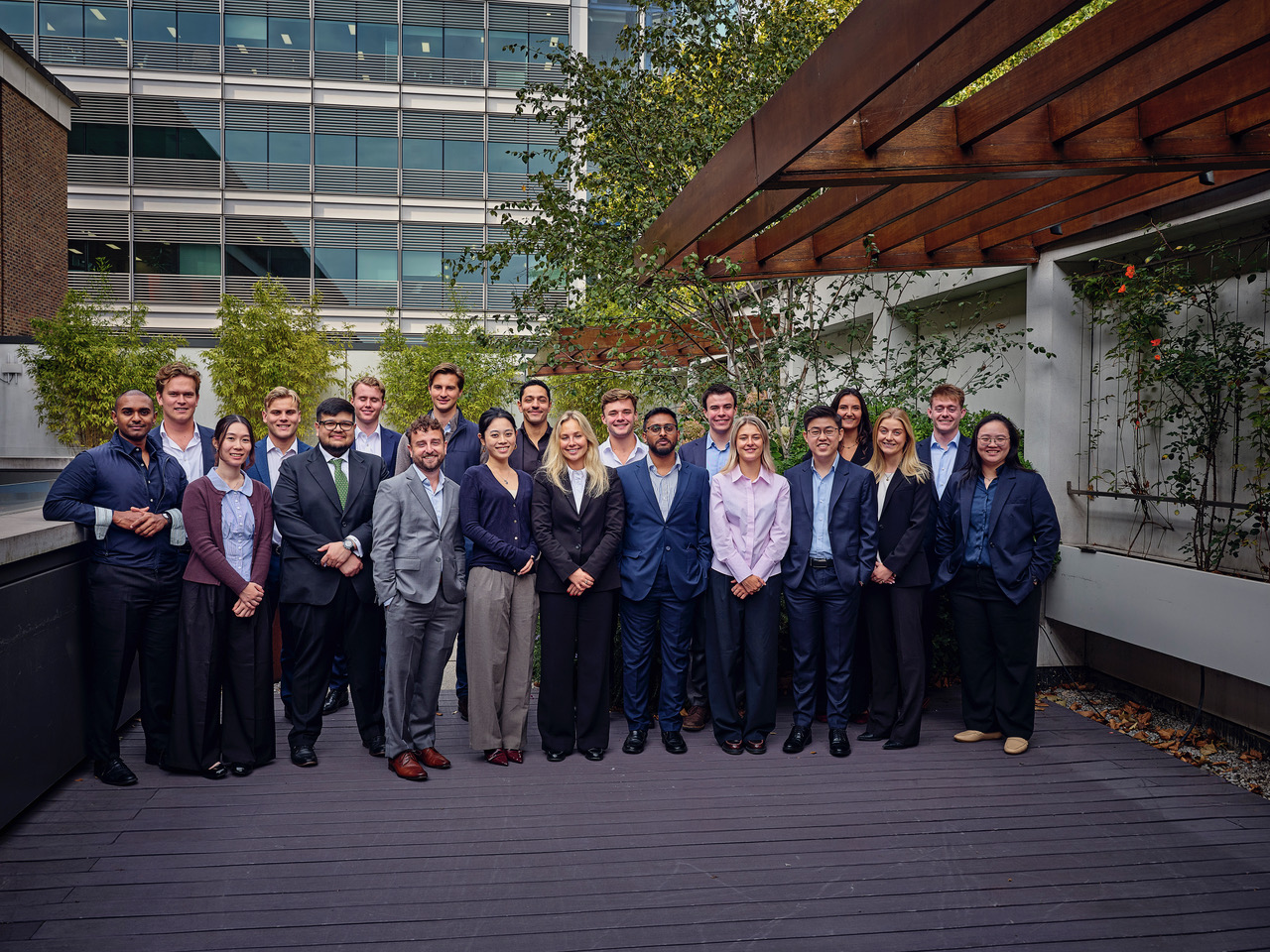 Group of 21 people in professional attire posing outdoors near a modern building.