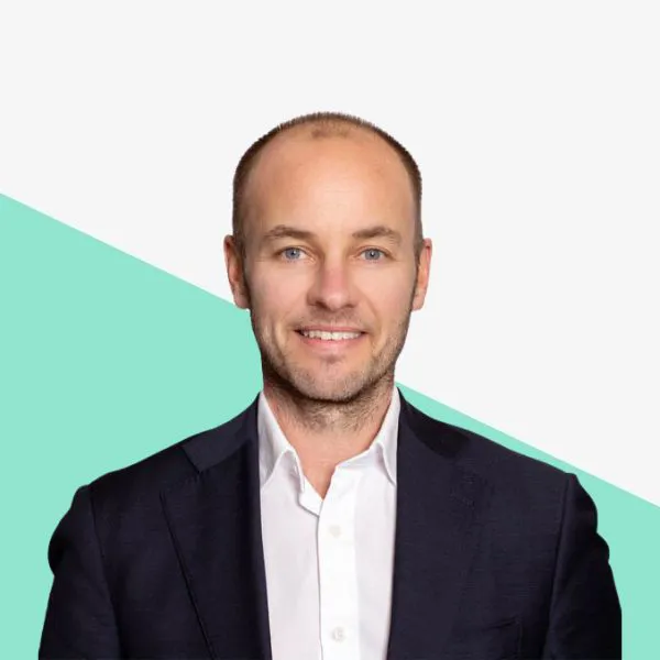Man in a suit smiling against a light background.