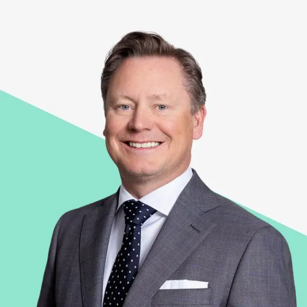 Man in a suit smiling against a light background.