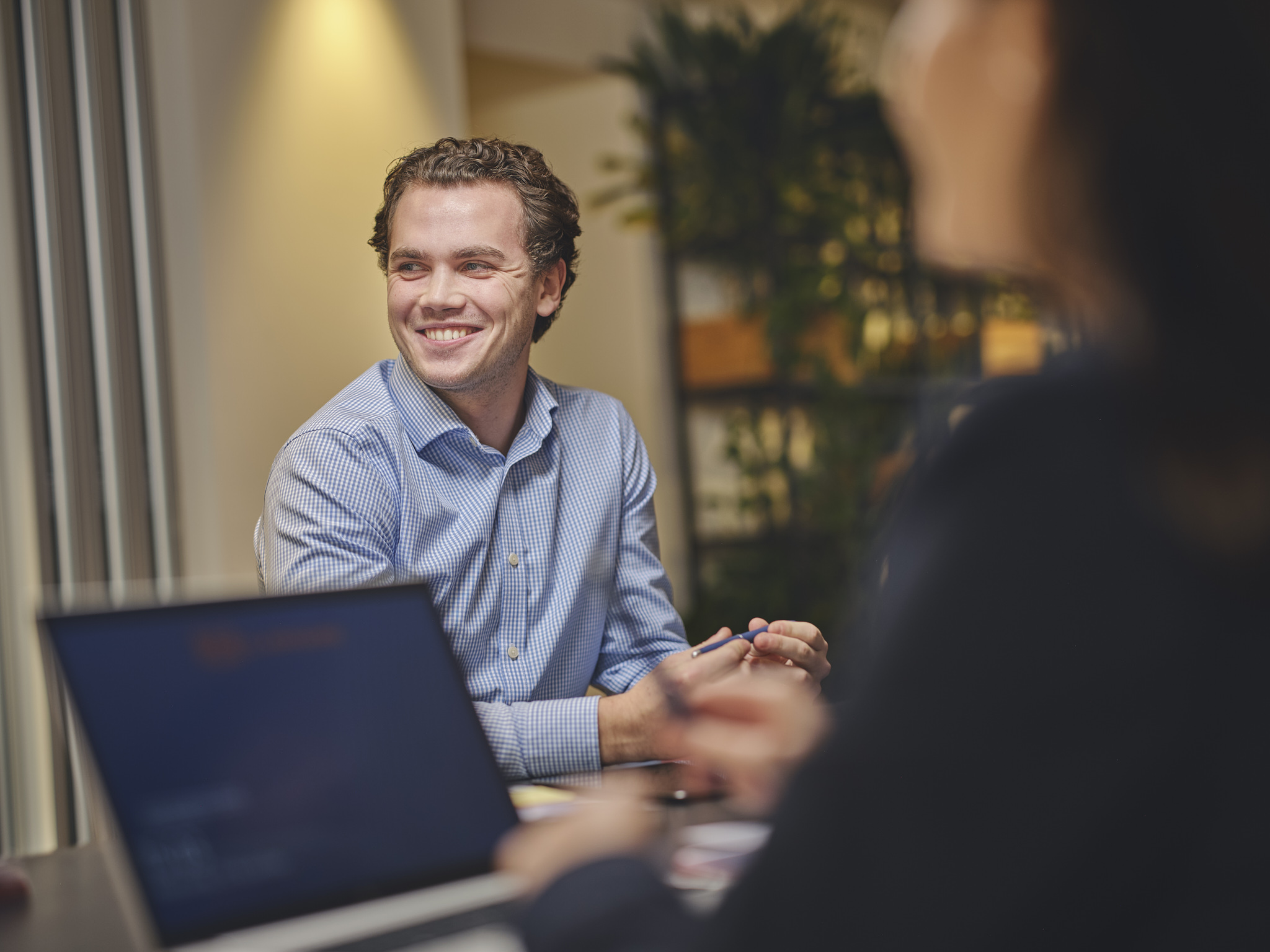 Smiling man in a meeting, laptop in foreground.
