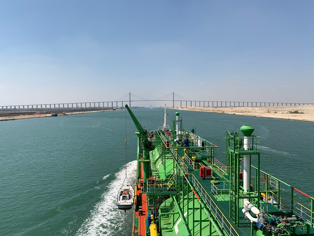 Green ship navigating a canal beneath a bridge.
