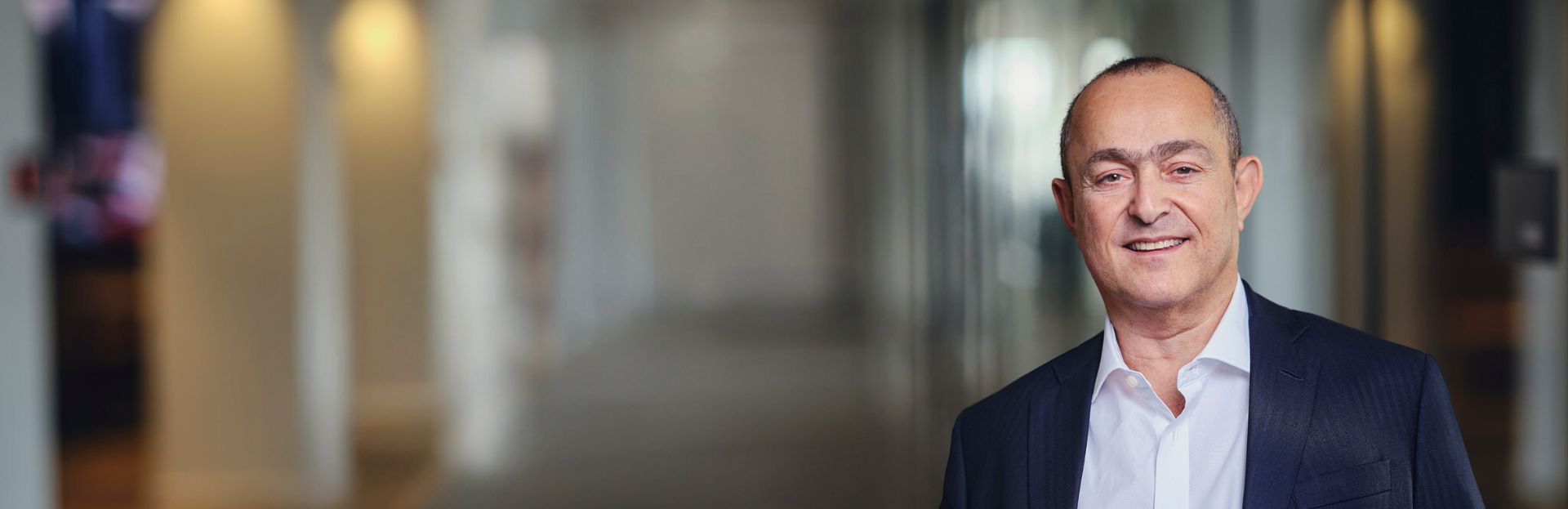 Smiling man in a suit, blurred indoor background.