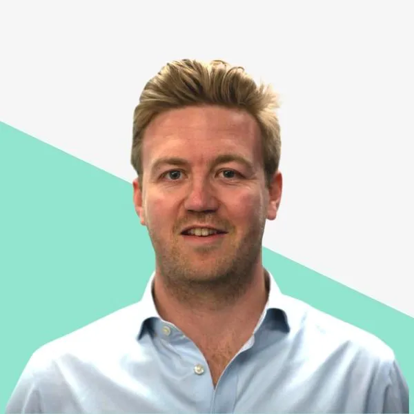 Man with light hair smiling against a simple background.