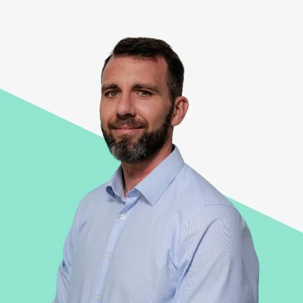 Man with a beard smiling against a light background.