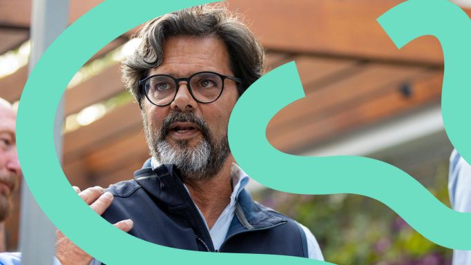 Man with glasses and beard gesturing outdoors.