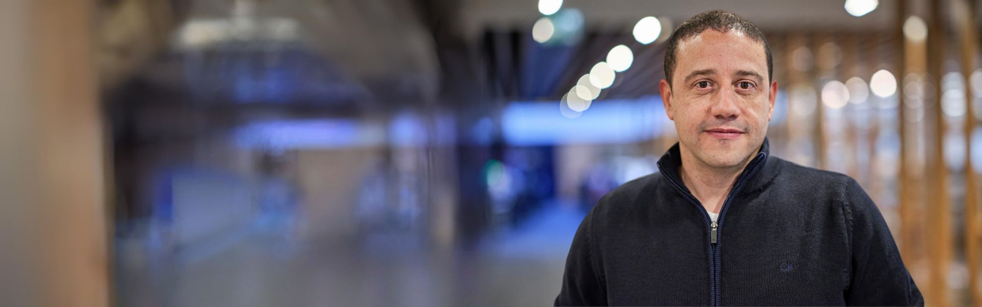 Man in a dark sweater standing in a hallway.