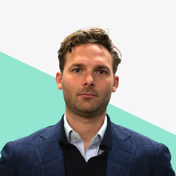 Man in a blazer against a teal and white background.