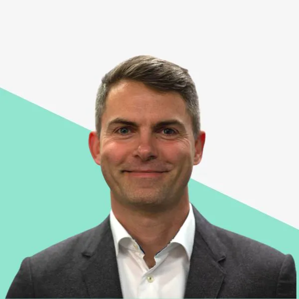 Man smiling in a suit, on a green geometric background.