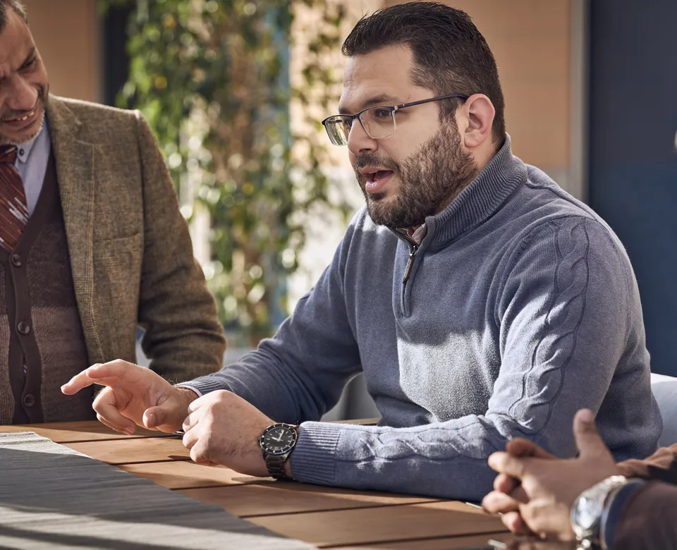 man sitting at a table talking to his colleagues and gesturing with his hands