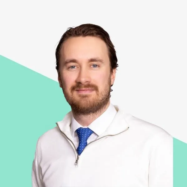 Man with beard in a white sweater and blue tie.
