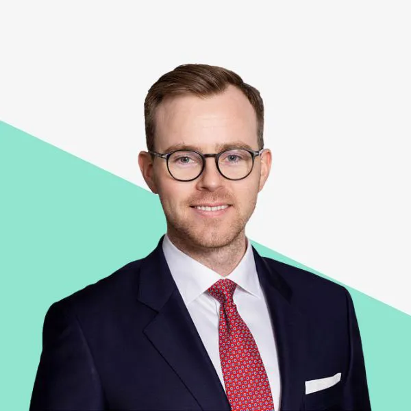 Man in a suit with glasses, smiling against a backdrop.