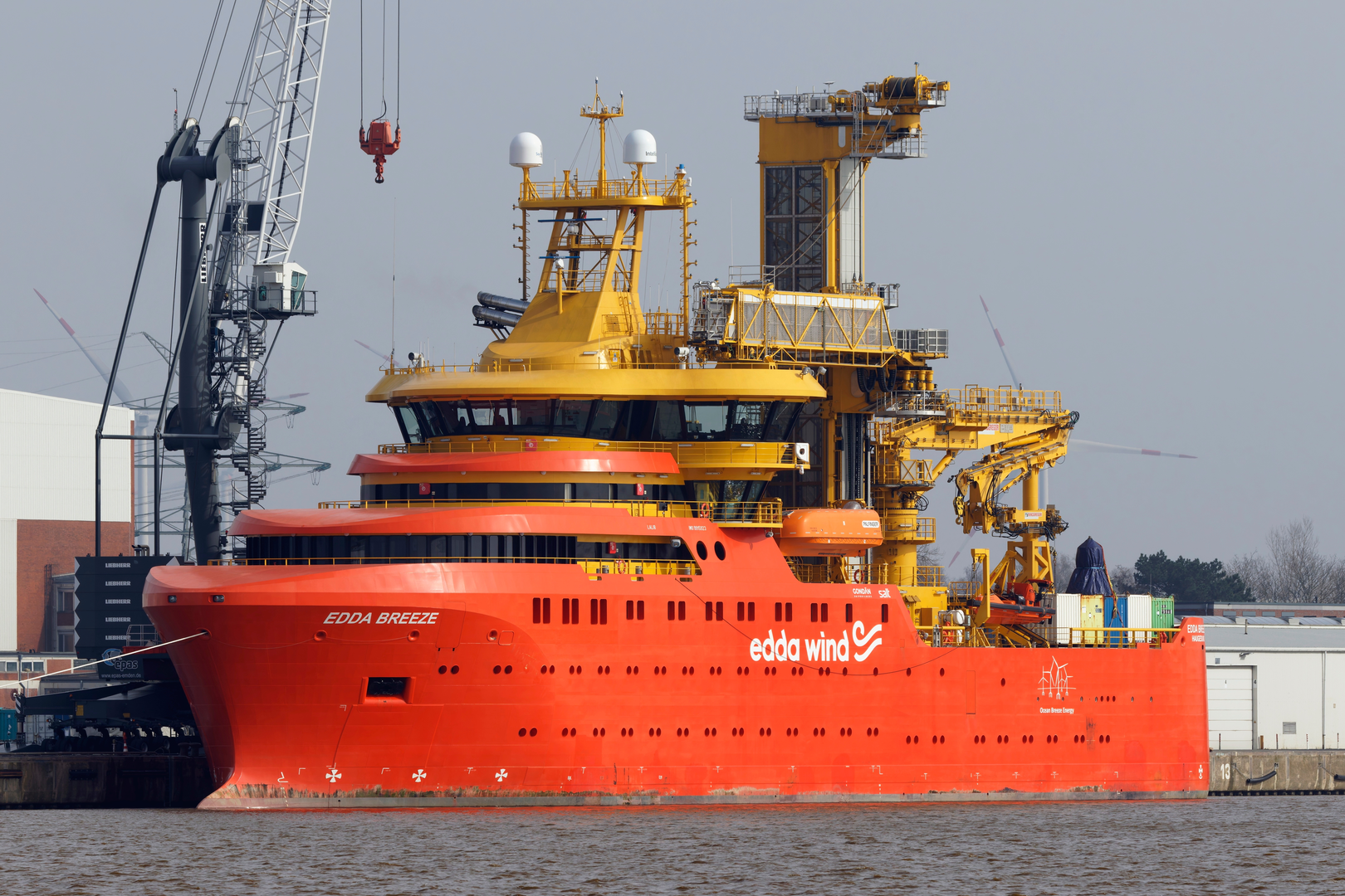 Large orange and yellow ship "Edda Breeze" docked at a port under an overcast sky.