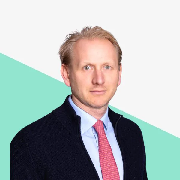 Man in a dark sweater and red tie on a light background.