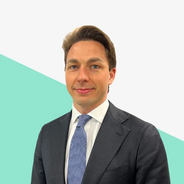 Man in a suit with blue tie, light background.