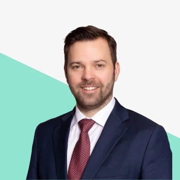Man in a suit smiling against a light background.