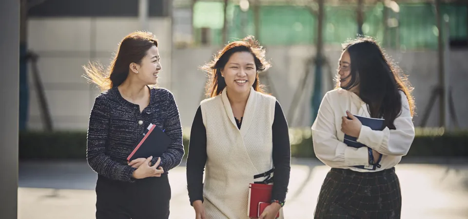 three women walking together outside and laughing, holding notes