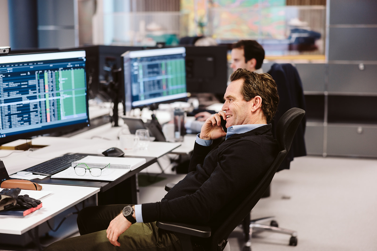 Man on phone in office, monitors with data screens.